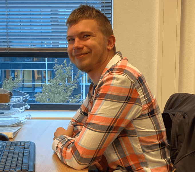 Servicedesk Engineer Mitch Dobbe zittend aan zijn bureau met een glimlach op zijn gezicht.